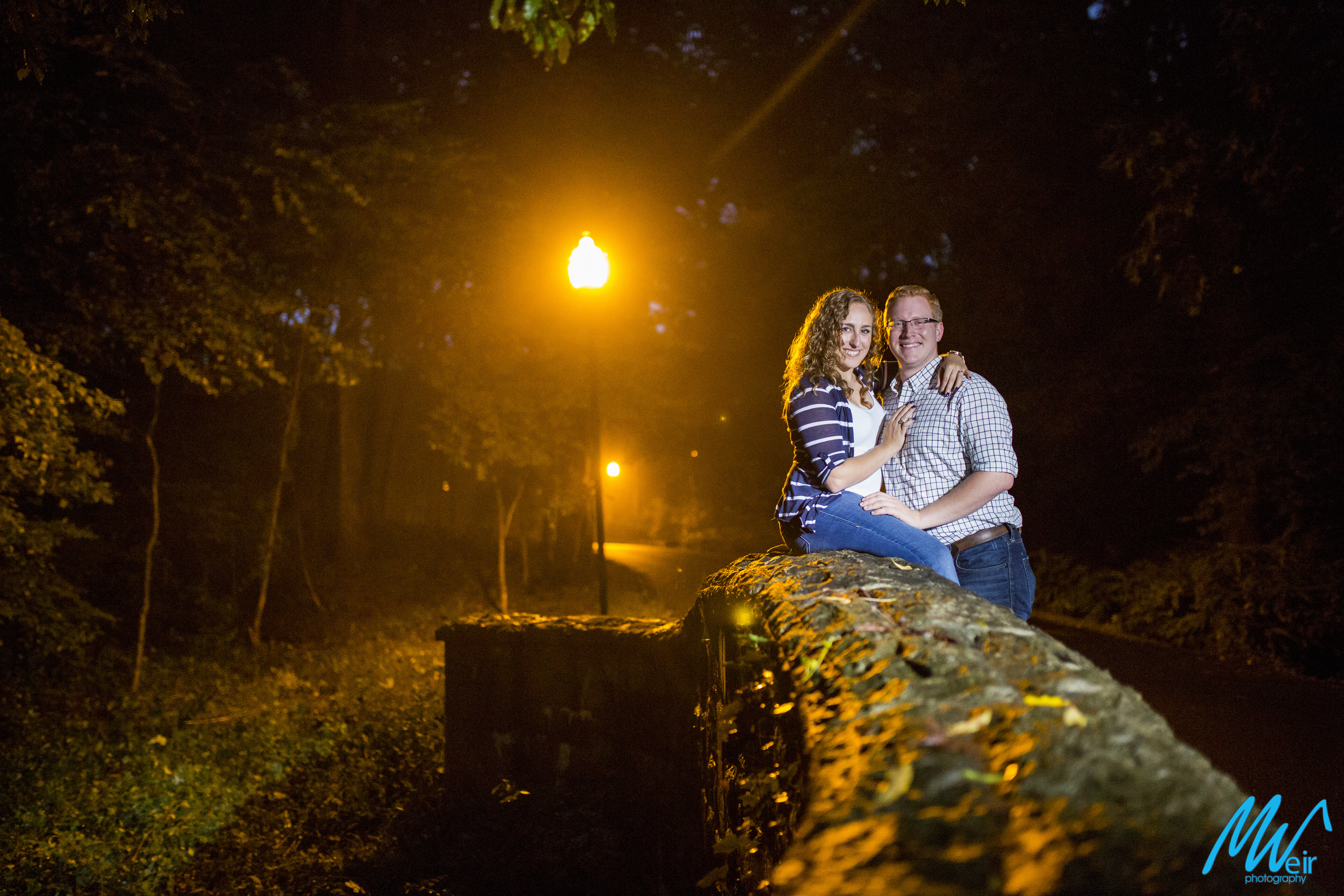 couple sit on a stone wall at night