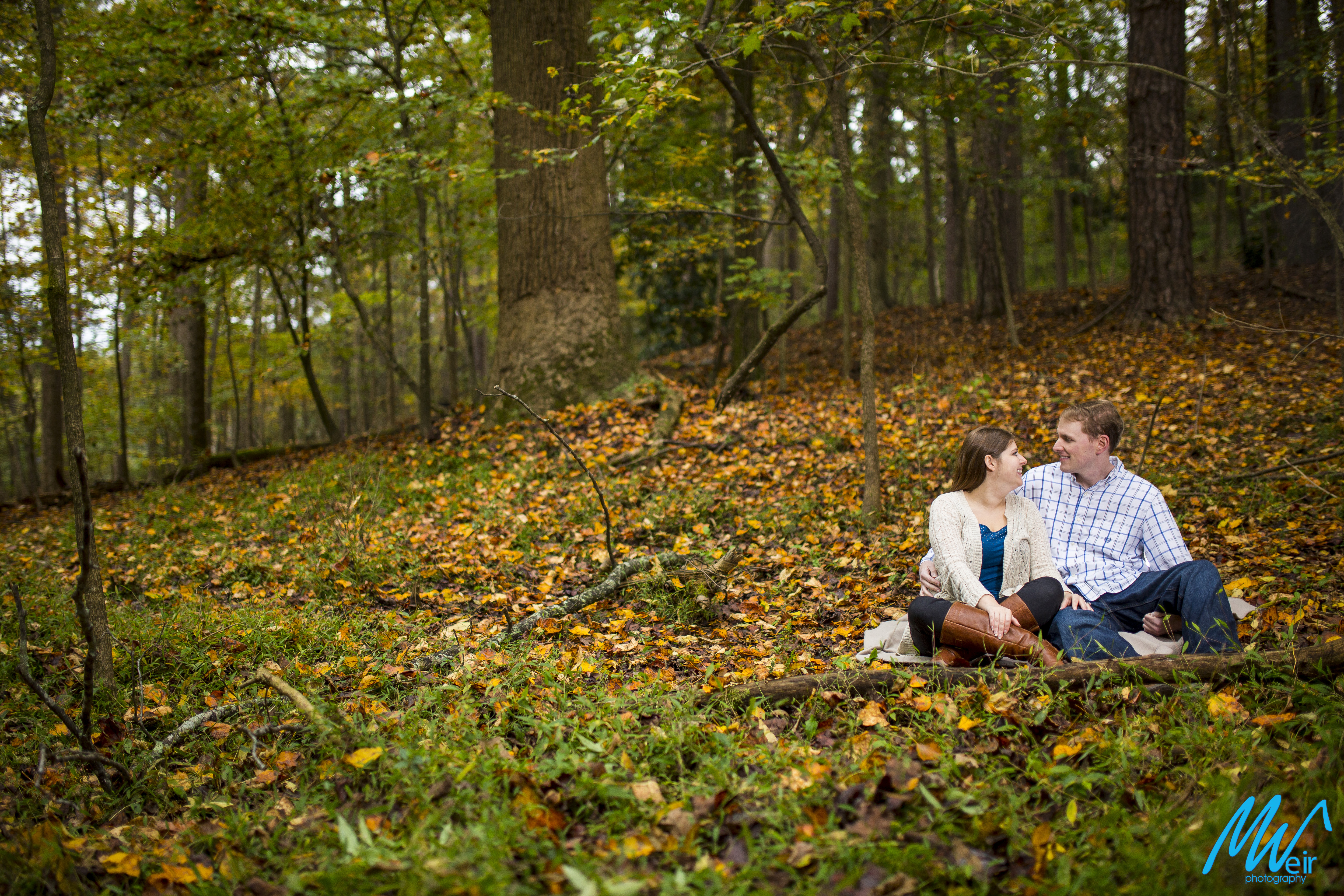 couple sit in the fall leaves in the woods