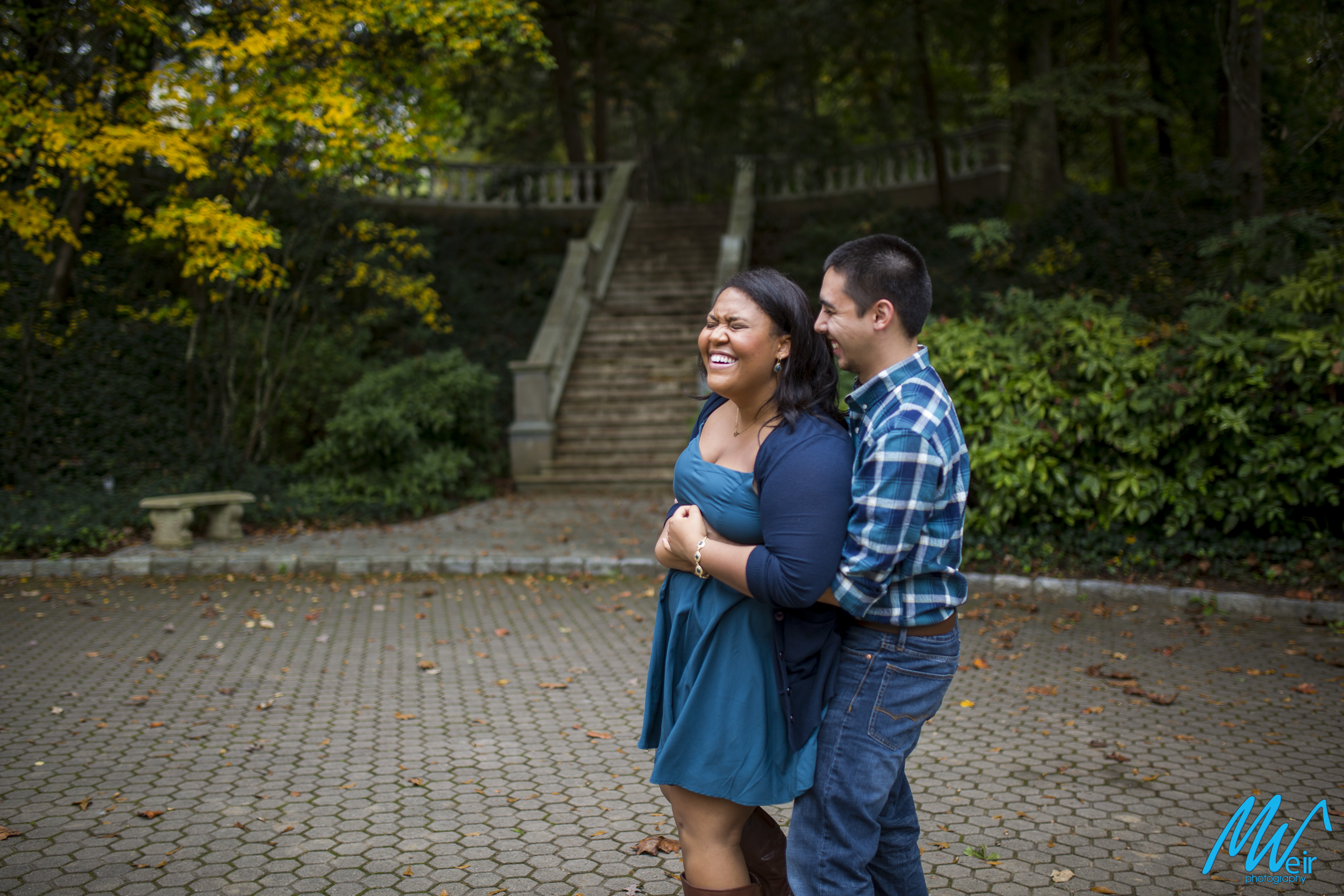 couple laugh together in cobblestone courtyard in front of grand stone staircase
