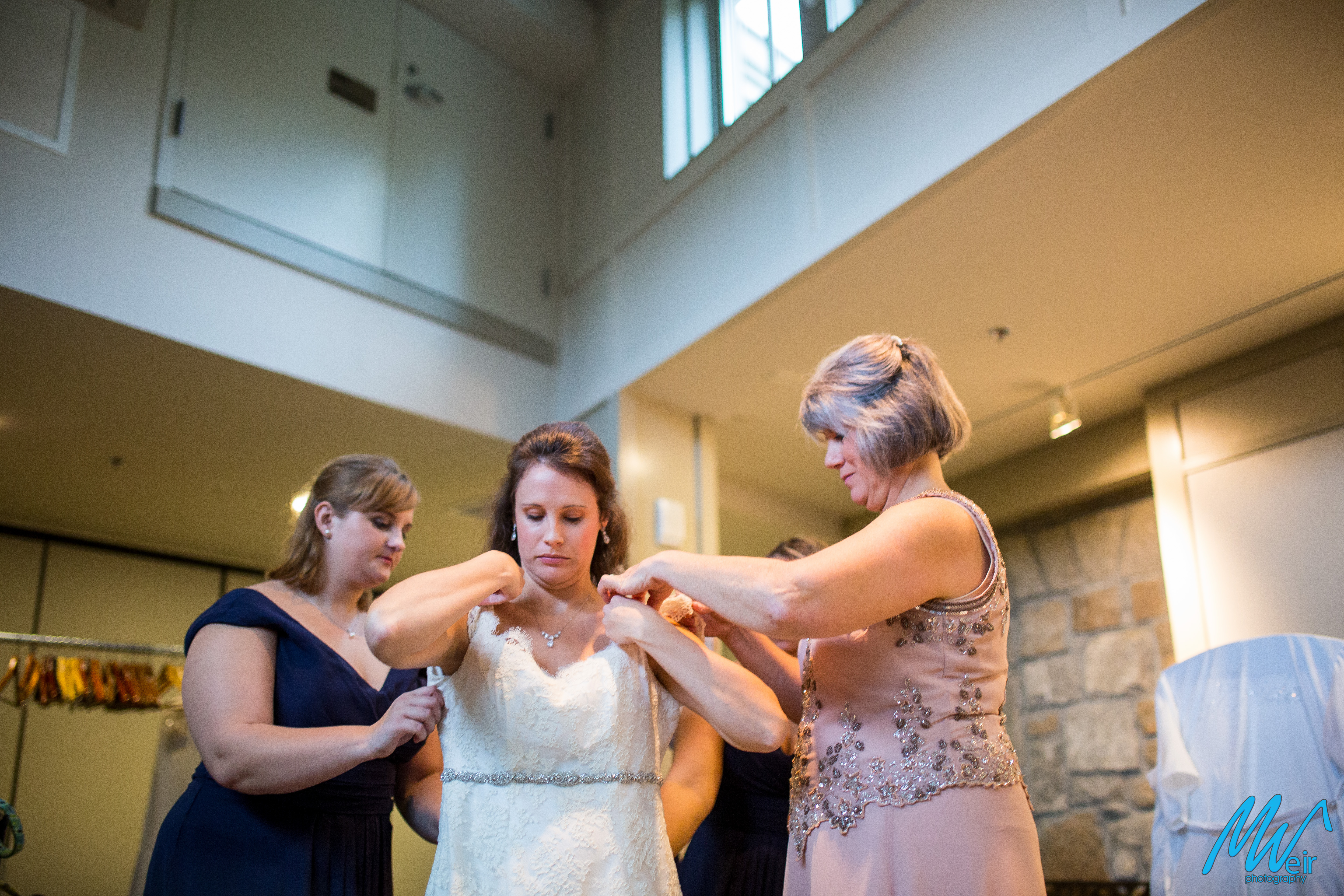 brides mom and sister helping her into her wedding dress